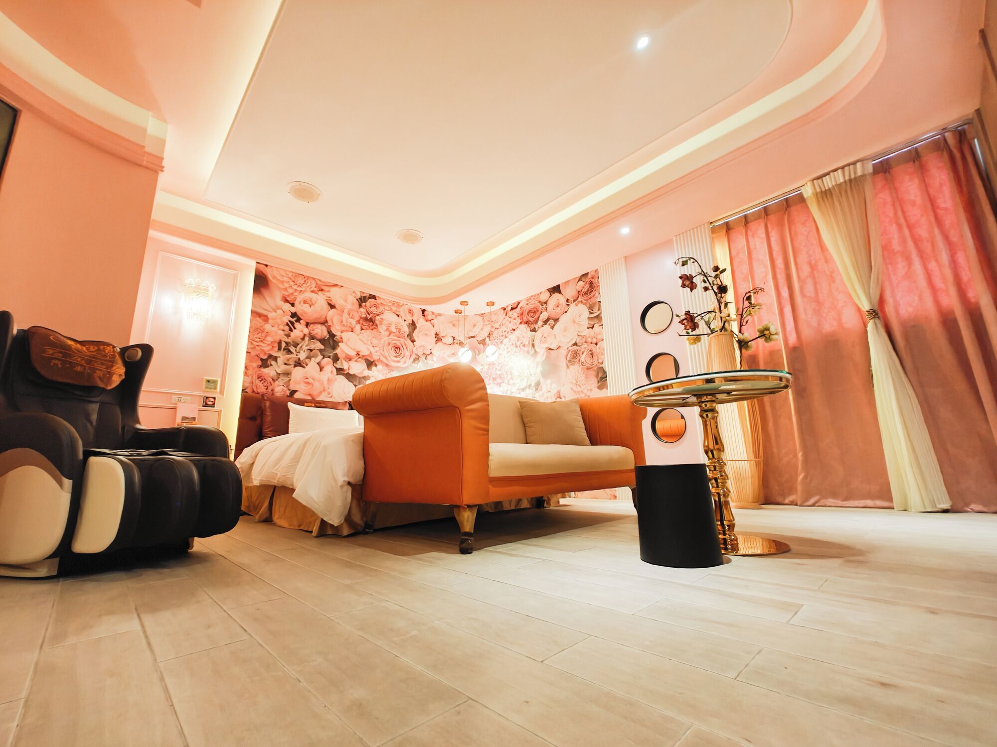 A modern living room with a sofa, a massage chair, a round table, and a floral wall mural.