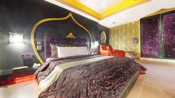 A modern bedroom with a large bed, a headboard with a decorative top, a red chair, and a wall-mounted TV.