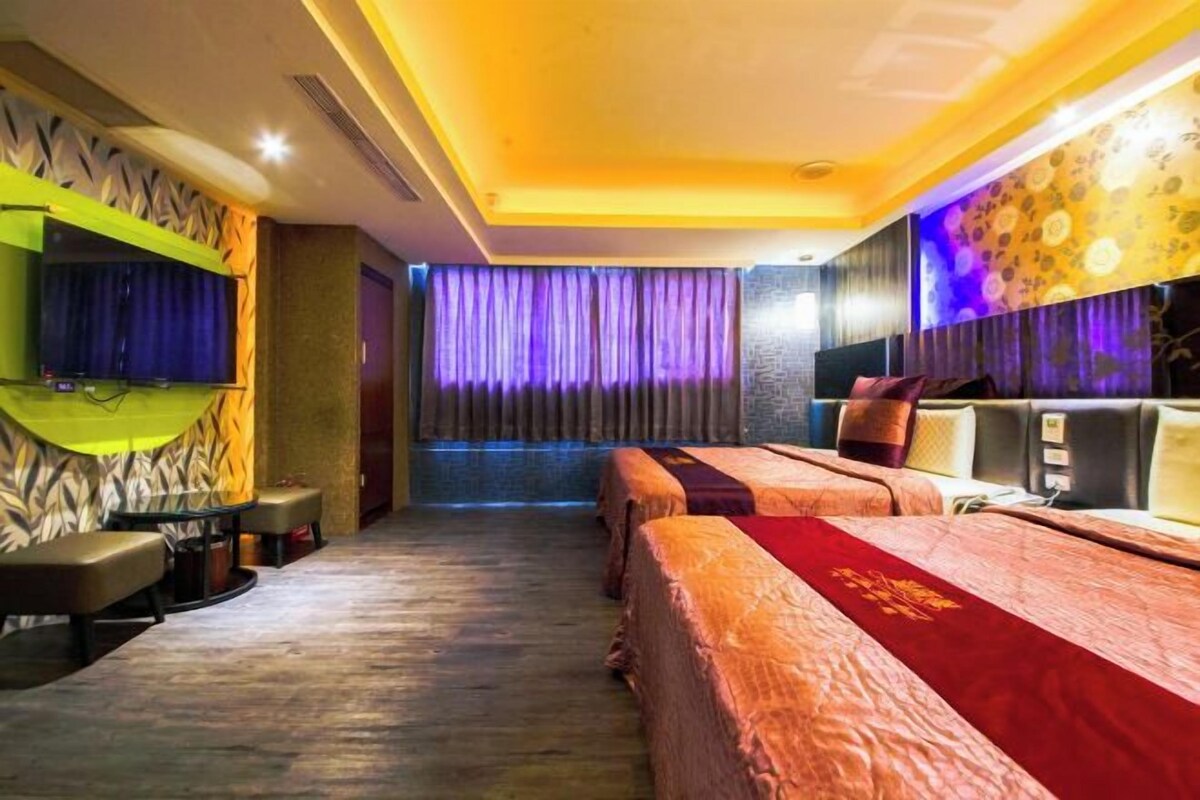 A hotel room with two beds, a television, a seating area, and a view of the street.
