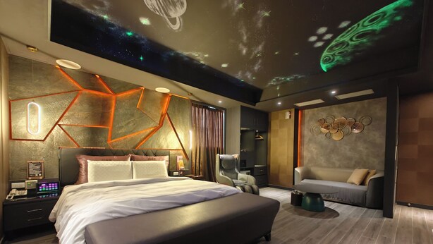 Un dormitorio moderno con una cama grande, un escritorio con computadora y una zona de estar con sofá y sillón.