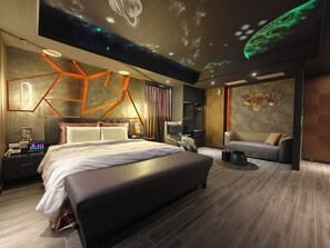 Une chambre moderne avec un grand lit, un bureau avec un ordinateur et un coin salon comprenant un canapé et un fauteuil.
