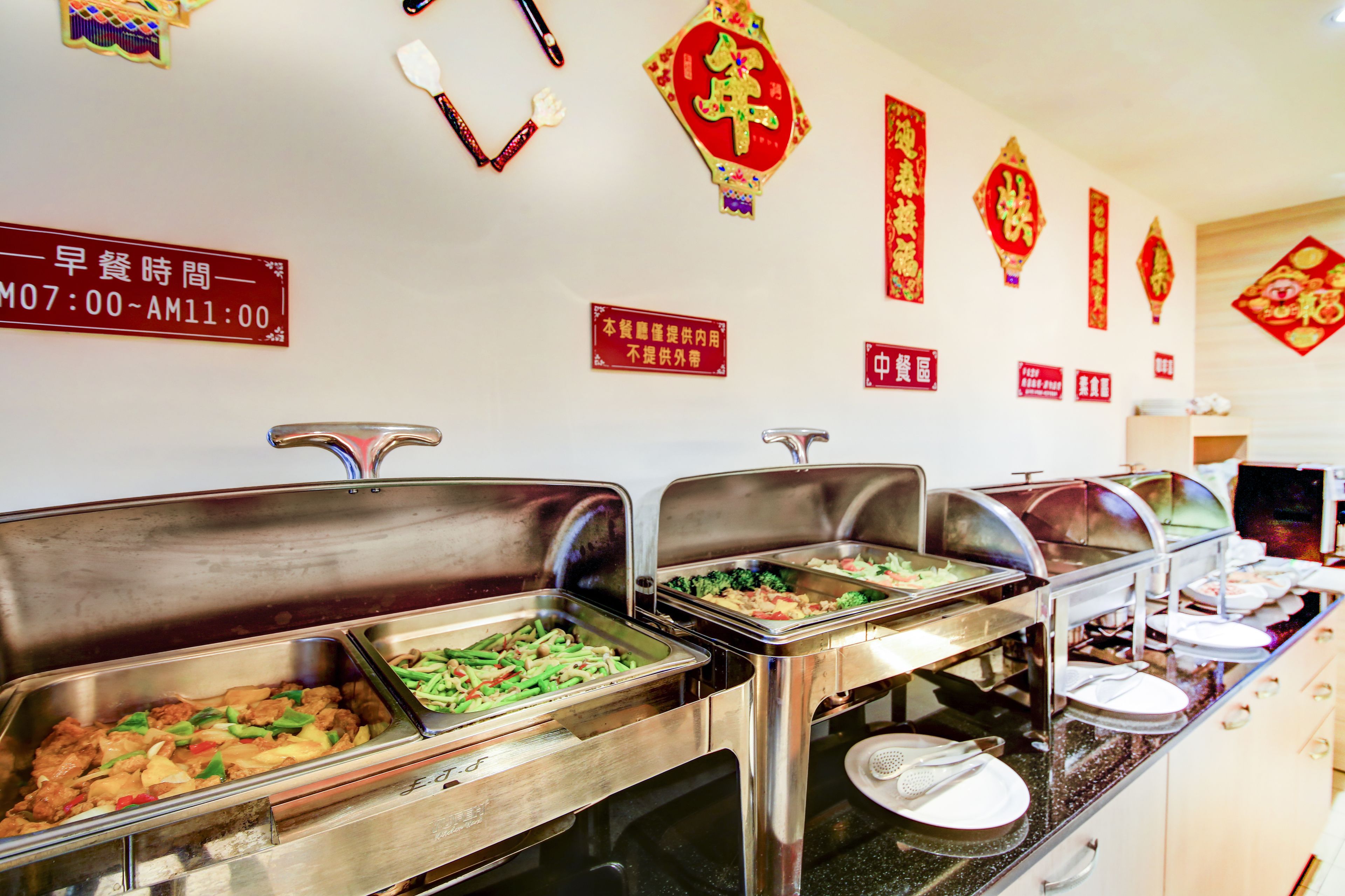 Zona de buffet amb diverses opcions gastronòmiques, estacions de servei d'acer inoxidable i penjolls decoratius xinesos.