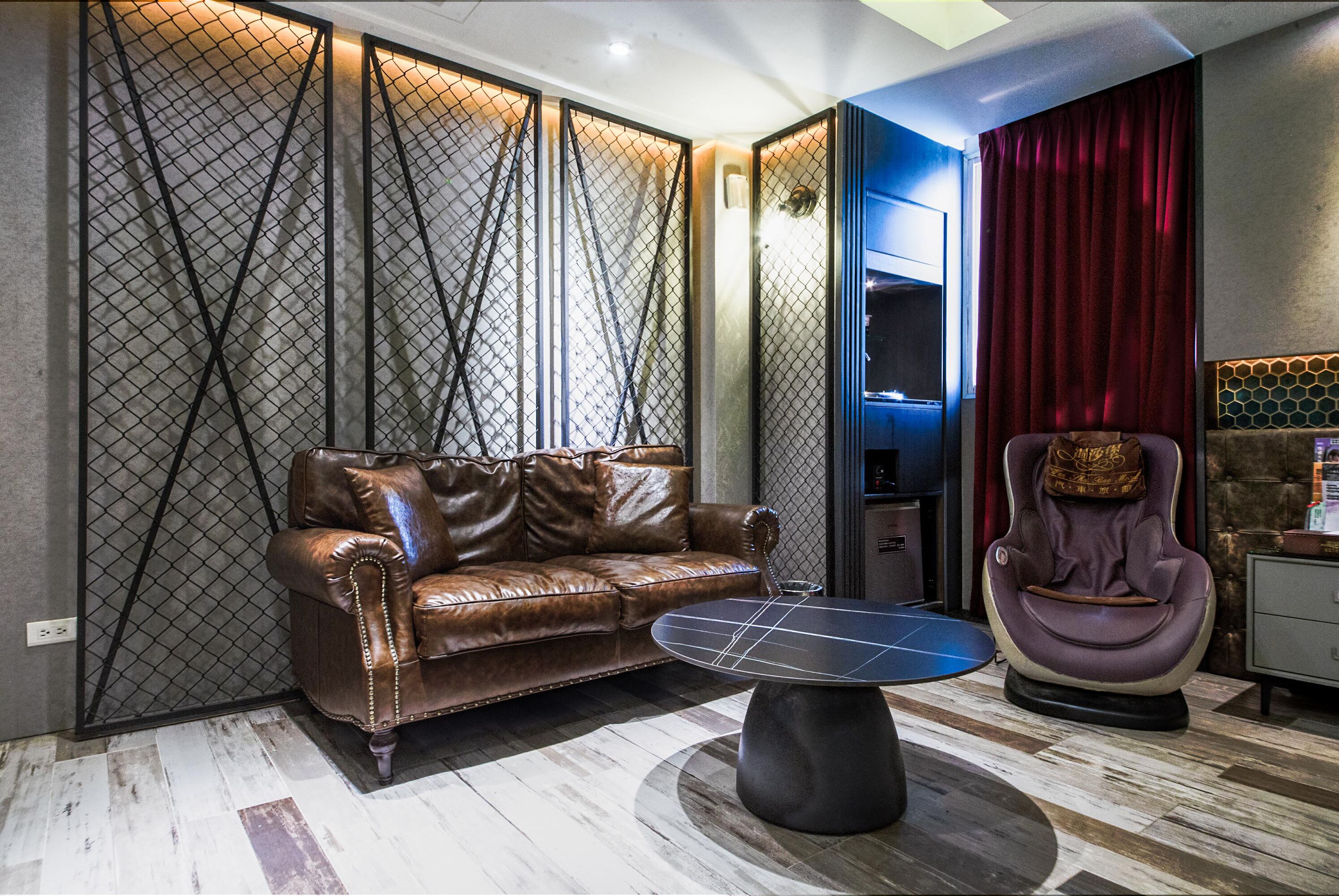 Een moderne woonkamer met een leren bank, een ronde salontafel, een massagestoel en een scheidingswand met een geometrisch patroon.