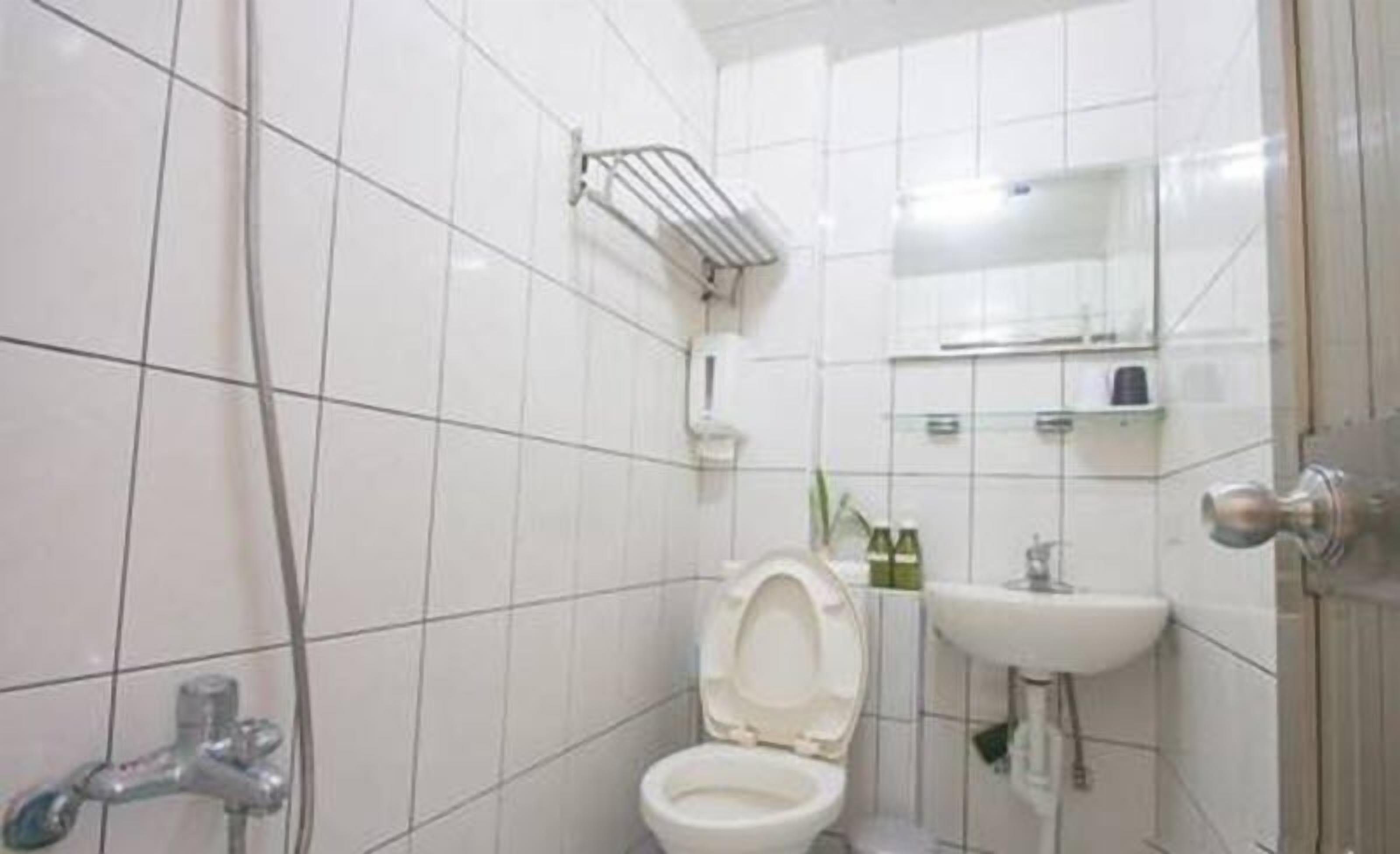 Une salle de bain avec des carreaux blancs, des toilettes, un lavabo et un espace douche.