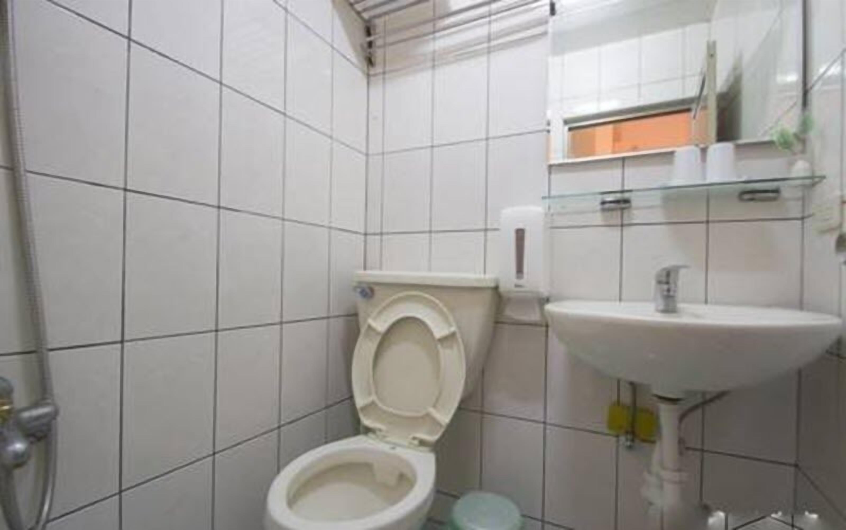 A small, tiled bathroom with a toilet, sink, and glass shower enclosure.