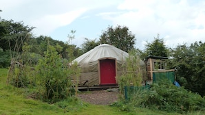 A single-story yurt with a red door, surrounded by dense greenery and a clear sky. - Yurt [sleeps up to 6] & Bathhouse in E Cornwall UK - 5* Off-Grid  (Callington)