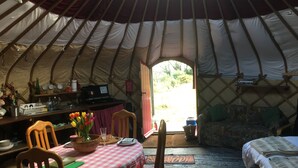 A cozy interior of a yurt with a dining area, a bed, and a small kitchen area. - Yurt [sleeps up to 6] & Bathhouse in E Cornwall UK - 5* Off-Grid  (Callington)