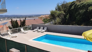 Piscina en la azotea con sillas de descanso y vista a una playa y montañas.