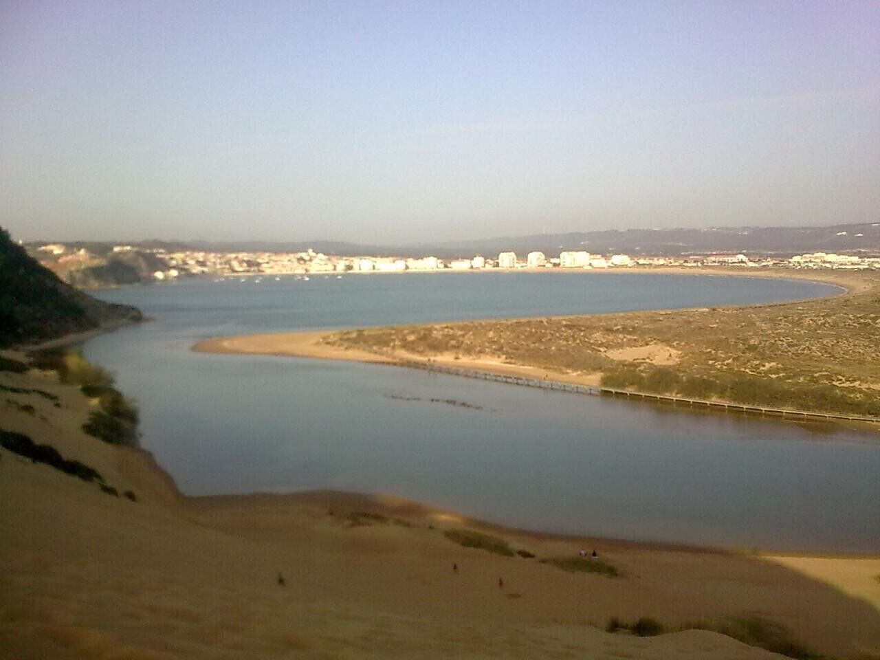 Un río con orilla arenosa y un paisaje urbano lejano.