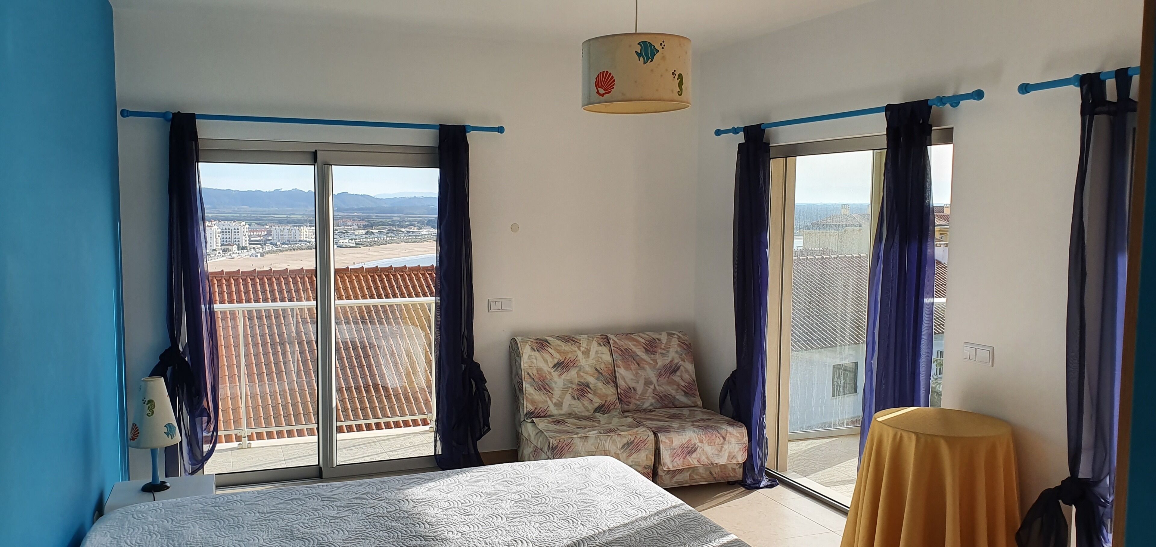 Une chambre à coucher avec un lit, une chaise, une table et une vue sur la ville grâce à de grandes fenêtres.
