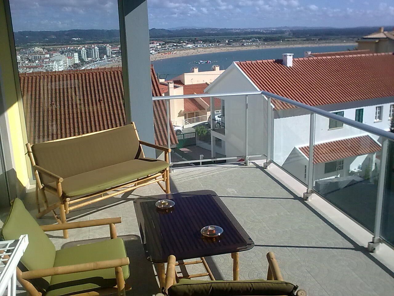 A balcony with a view of a coastal cityscape, featuring a table and two chairs.