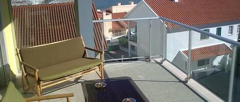 A balcony with a view of a coastal cityscape, featuring a table and two chairs.