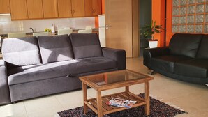 Una sala de estar con un sofá gris, un sillón negro y una mesa de centro de vidrio.