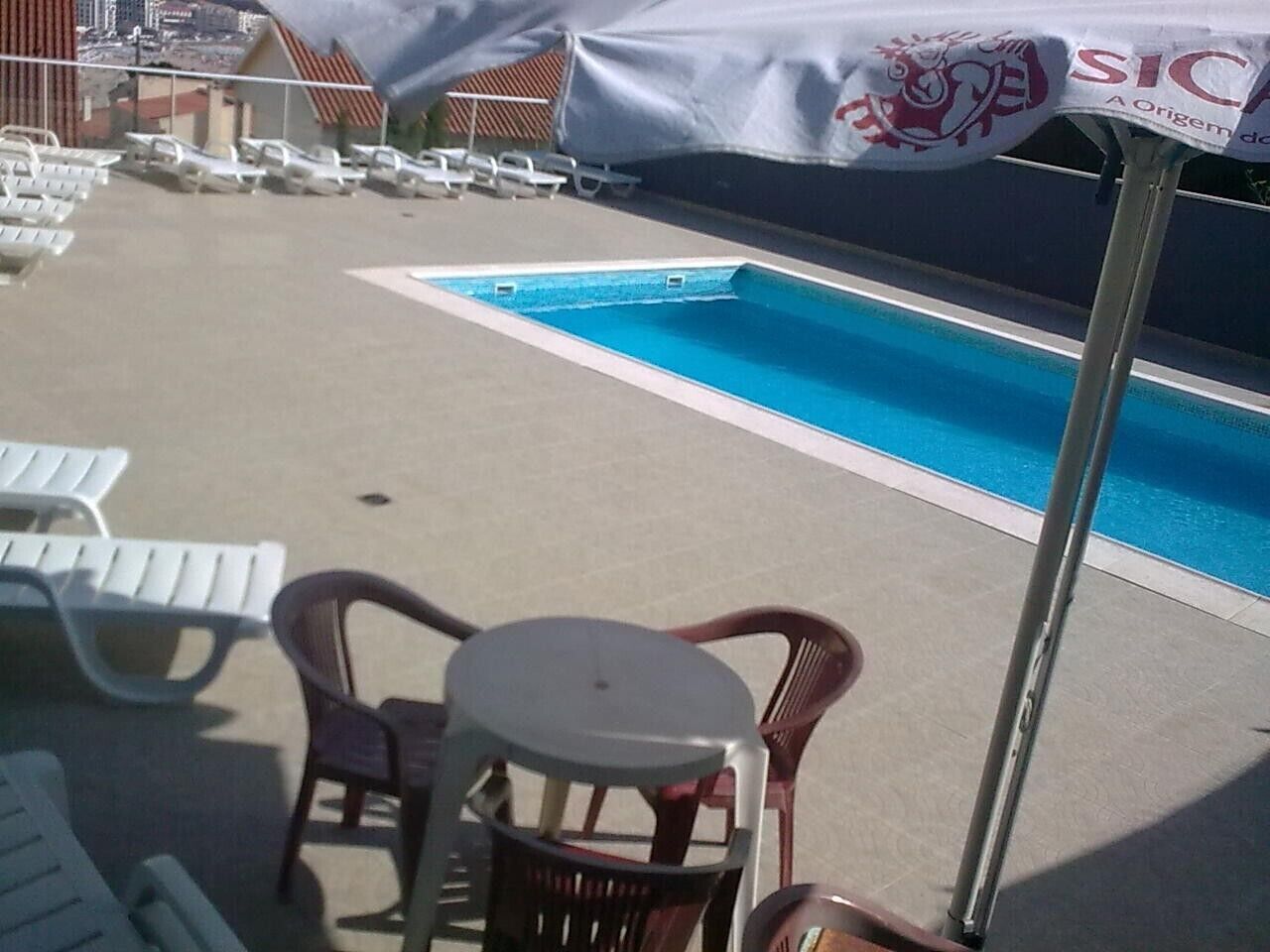 Un espace piscine avec des chaises longues et une table placée sous un parasol.