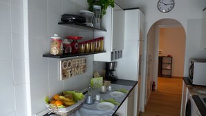 A kitchen with white tiled walls, a coffee sign, shelves with jars and kitchen appliances, a dining table set with plates and cutlery, and a clock on the wall. - Your Home @ ROME near TRASTEVERE (Roma)