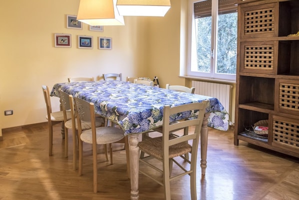 A dining area with a table covered in a floral tablecloth, surrounded by wooden chairs.