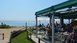 Ein Sitzbereich im Freien mit Tischen und Stühlen mit Blick auf einen Strand und das Meer.