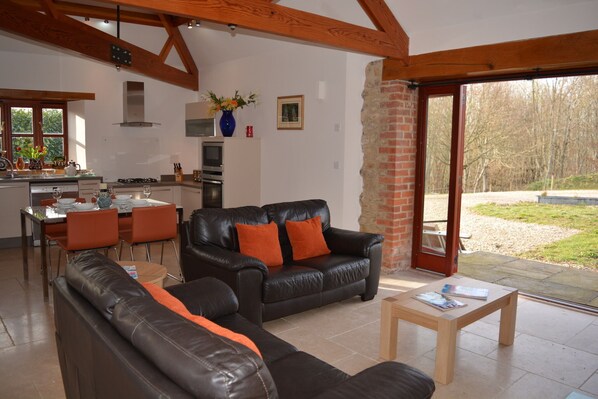 A spacious living area with a black leather sofa, a wooden coffee table, and a dining area with orange chairs.