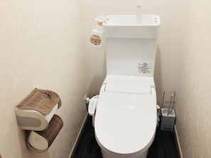 A toilet with a white seat and lid, a toilet paper holder, and a bidet spray bottle. - Midtown Sakura Apartment House 102 (Nachikatsuura)