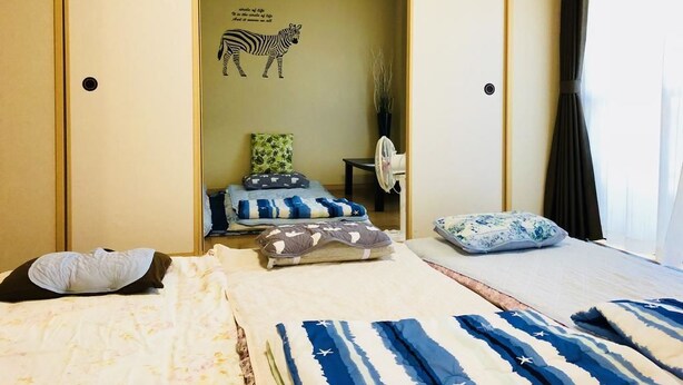 A hotel room with two beds, a zebra wall decal, a small table with a fan, and a window with curtains.