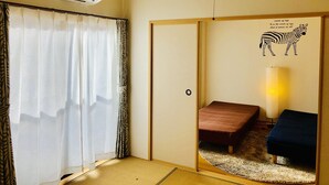 A room with a sliding door, a bed, a bedside table, a lamp, and a wall decal of a zebra. - Midtown Sakura Apartment House 101 (Nachikatsuura)