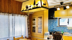 A compact kitchen with a dining area, featuring a wooden table, chairs, a buffet cabinet, and a window with a view of the outdoors. - Midtown Sakura Apartment House 101 (Nachikatsuura)