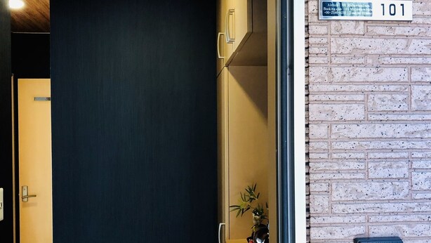 A hotel room with a dark door, a small plant on the counter, and a brick wall. - Midtown Sakura Apartment House 101 (Nachikatsuura)