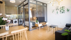 A modern living space with a dining area, a sofa, a TV, and a kitchen area visible through a glass partition. - Cuu Kim Son Hotel (Ho Chi Minh City)