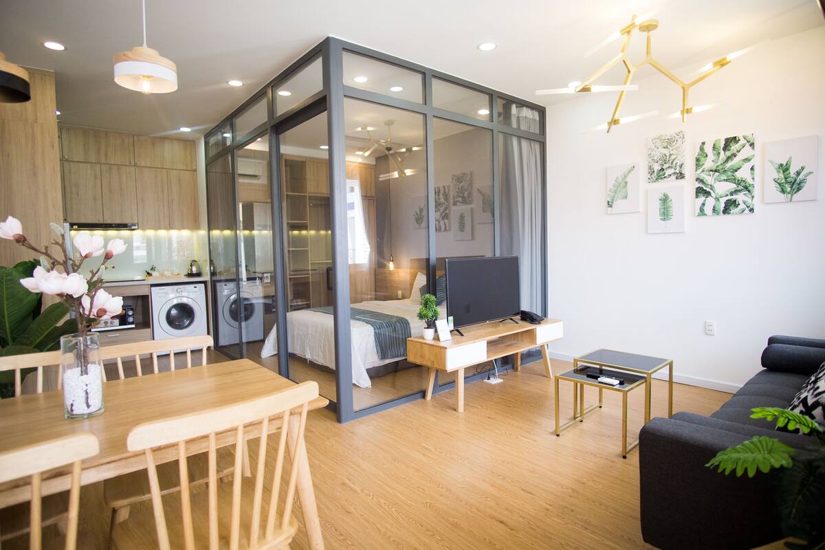 A modern living space with a dining area, a sofa, a TV, and a kitchen area visible through a glass partition.