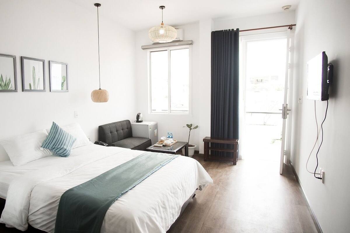 A hotel room with a bed, a desk, a chair, a window with curtains, and wall-mounted artwork.