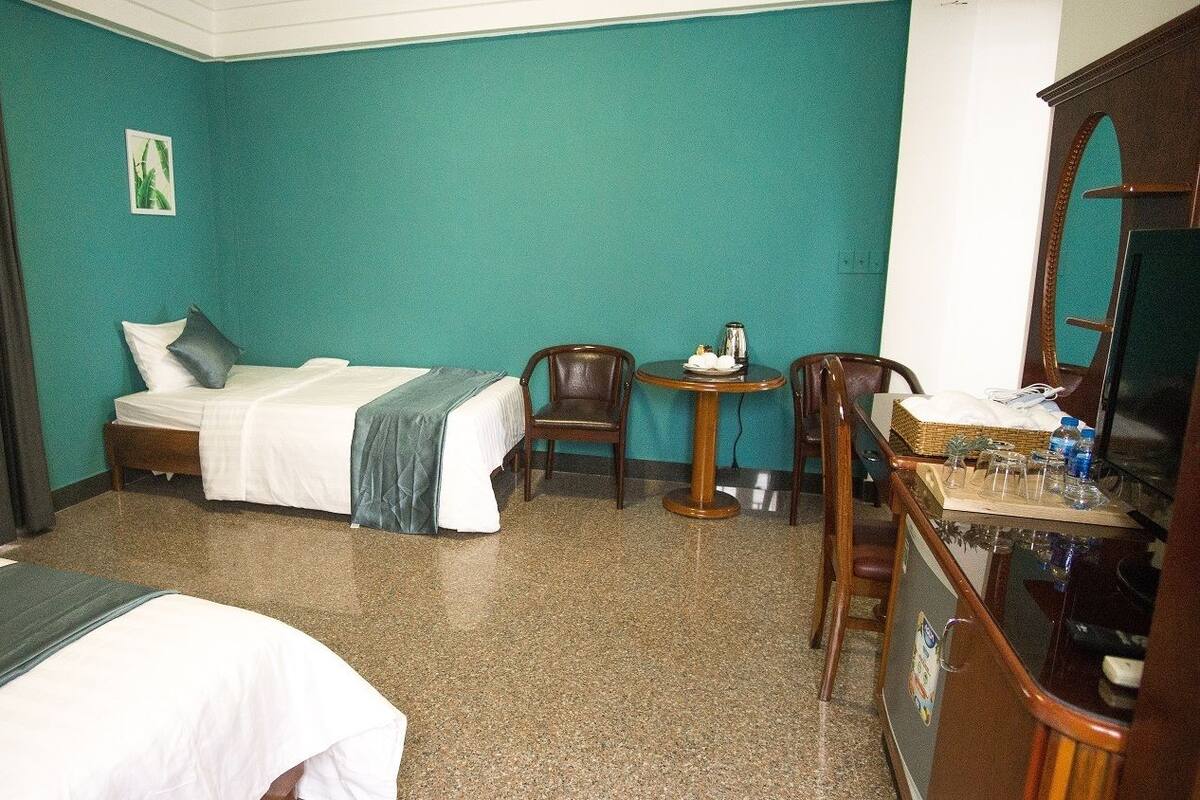 A hotel room with a bed, a desk with a chair, a small table with a kettle, and a television.