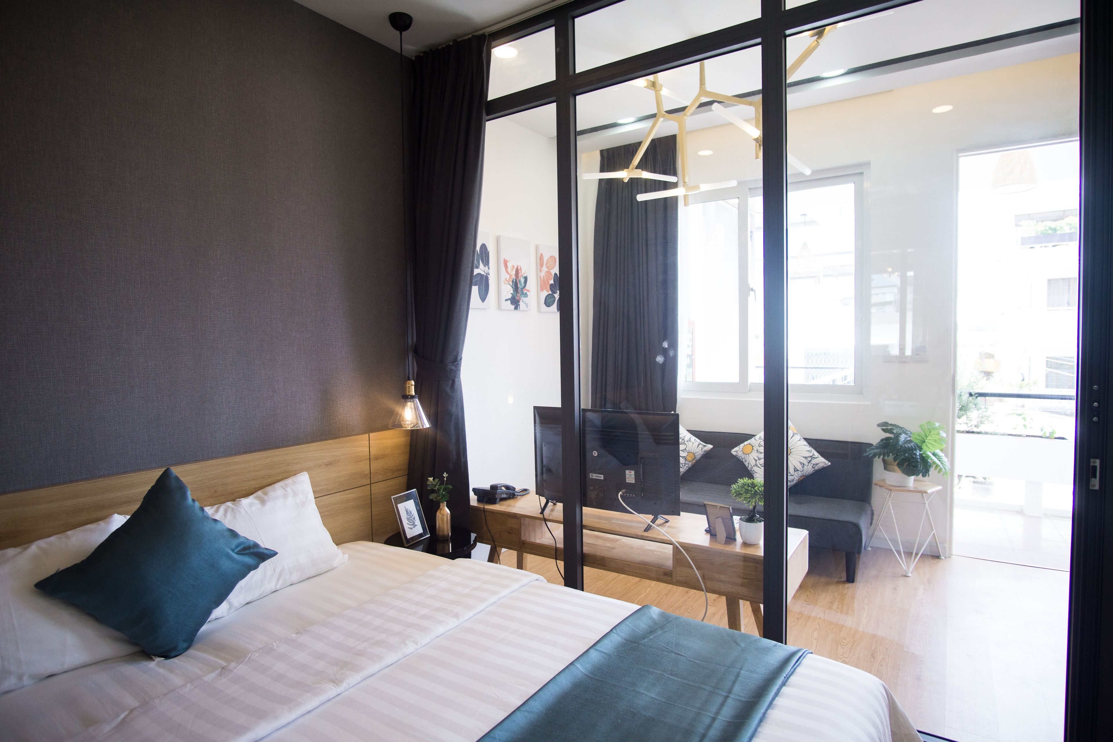 A modern hotel room with a large bed, a desk with a computer, and a view of the city through large windows.