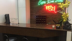 A hotel reception desk with a neon sign, a small Buddha statue, and a yellow orchid arrangement. - Cuu Kim Son Hotel (Ho Chi Minh City)