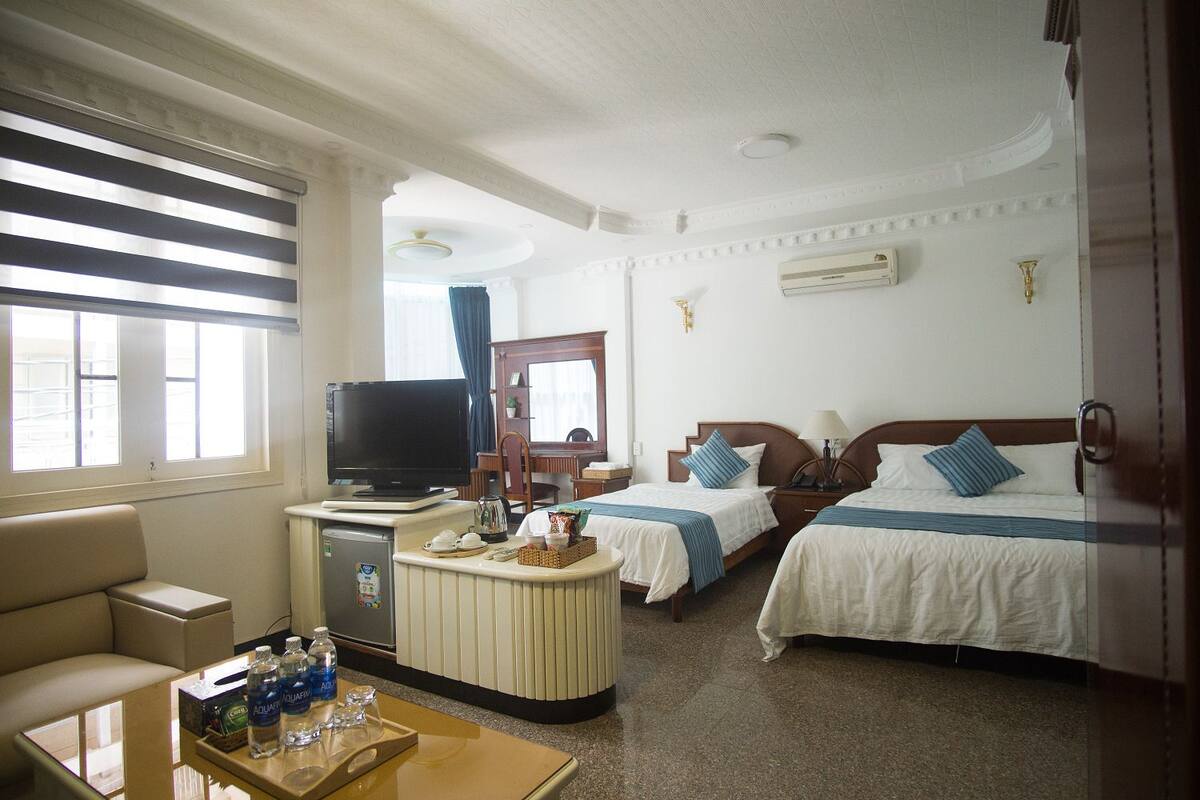 A hotel room with two beds, a television, a desk with a computer, and a window with blinds.
