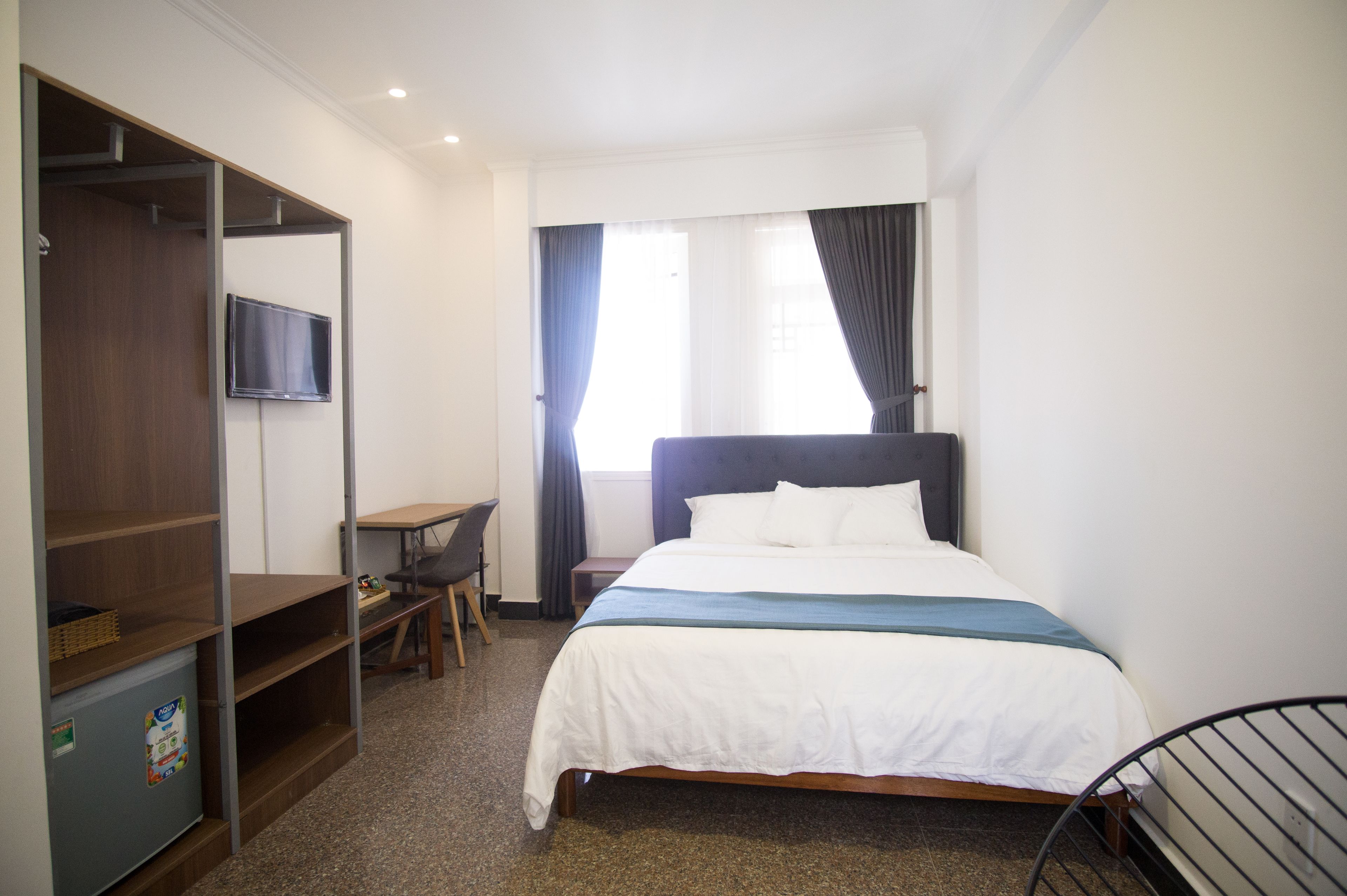 A hotel room with a bed, a TV mounted on the wall, a desk, and a chair.