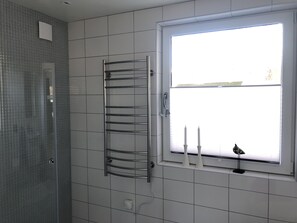 Une salle de bain avec un mur carrelé, une fenêtre décorée de bougies blanches et un porte-serviettes.