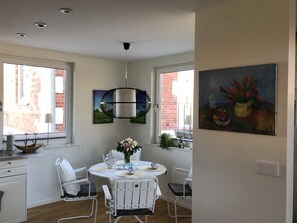 Un coin repas avec une table ronde, des chaises blanches, un luminaire suspendu et des œuvres d’art accrochées aux murs.