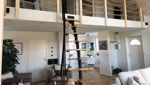 Een ruime loft met een centraal geplaatst trap, hoge plafonds en een entresol.
