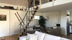 Een ruime woonkamer met een witte bank, een houten trap en een keuken op de achtergrond.