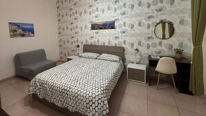A bedroom with a bed, a desk, a chair, a nightstand, a mirror, and a wall with a circular pattern.