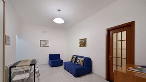 A room with a dining table, chairs, a blue sofa, a wooden door, and a ceiling light fixture.