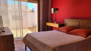 Une chambre à coucher avec un lit, un bureau, une lampe et une vue sur l’extérieur.
