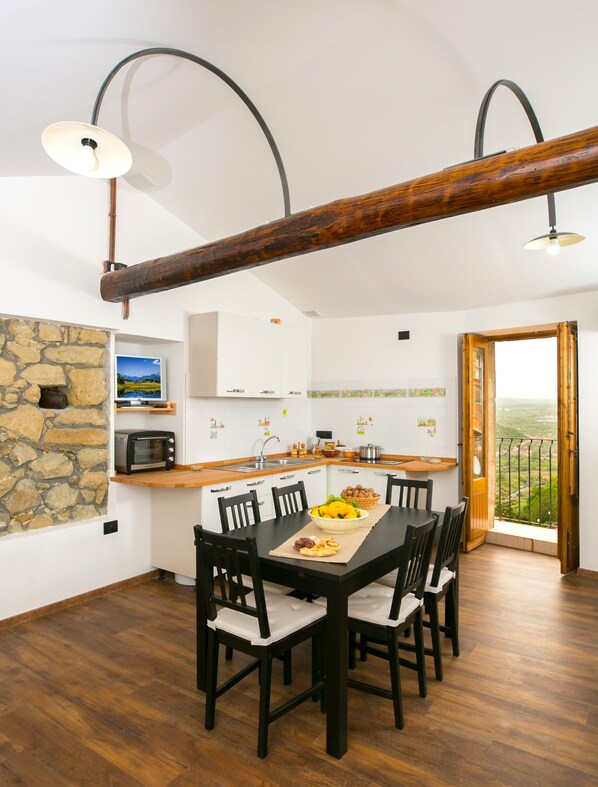 A modern kitchen with a stone wall, wooden beams, and a dining area with a table set for four.