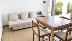 A room with a wooden dining table, four chairs, a white sofa with cushions, and a view of greenery outside. - M051 - Marcelli, villa with garden 200 meters from the sea (Marcelli)