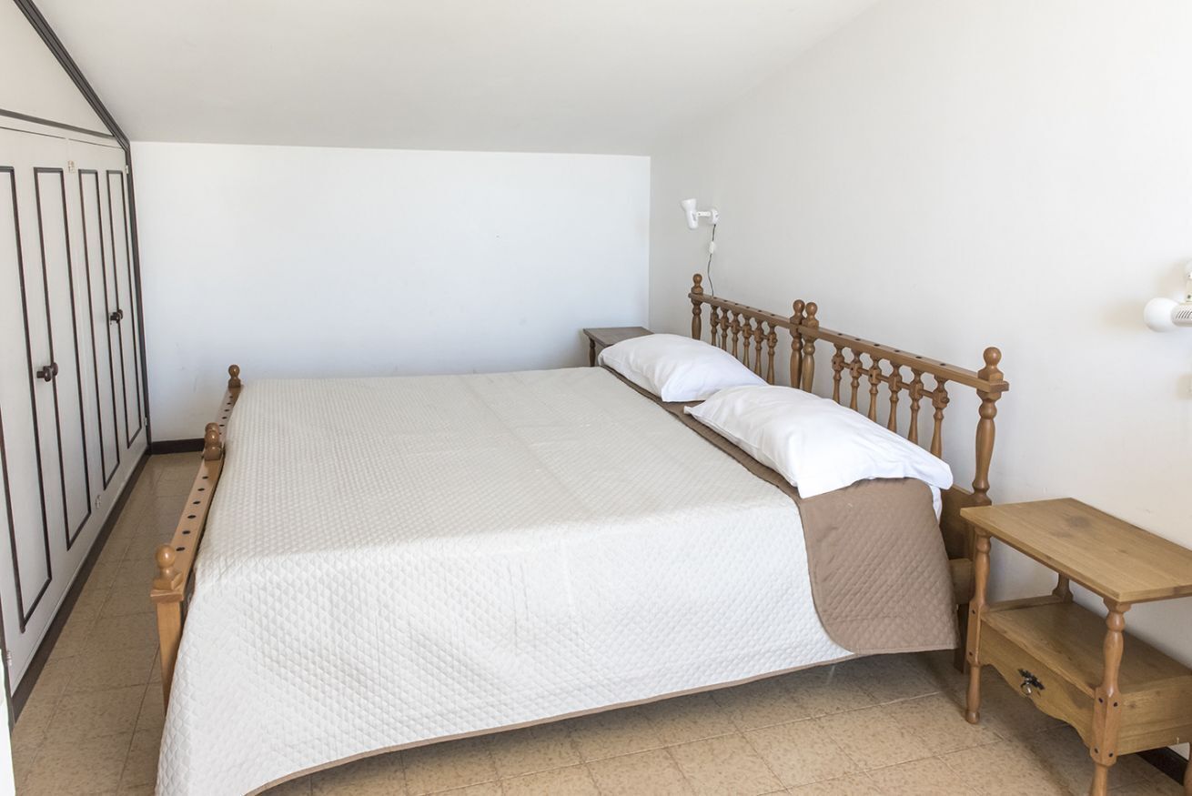 A single bed with a wooden headboard, a bedside table, and a wardrobe with a mirror.