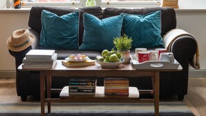 Un salon chaleureux avec un canapé, des coussins turquoise, une table basse avec des livres, un chapeau, un vase de fleurs et un plateau avec des tasses et une théière.