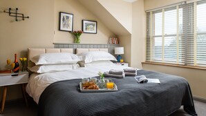 Un lit bien fait, avec du linge de lit blanc, un plateau de petit-déjeuner et une table de chevet avec une lampe et des livres.