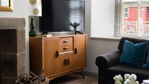 Un salon comprenant un meuble en bois, un téléviseur à écran plat, une cheminée, un canapé et une fenêtre avec des stores.