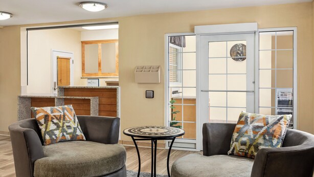 A modern living room with two grey armchairs, a small round table, and a sliding glass door leading to a balcony. - Candlewood Suites Augusta (Augusta)