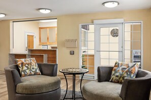 A modern living room with two grey armchairs, a small round table, and a sliding glass door leading to a balcony. - Candlewood Suites Augusta (Augusta)